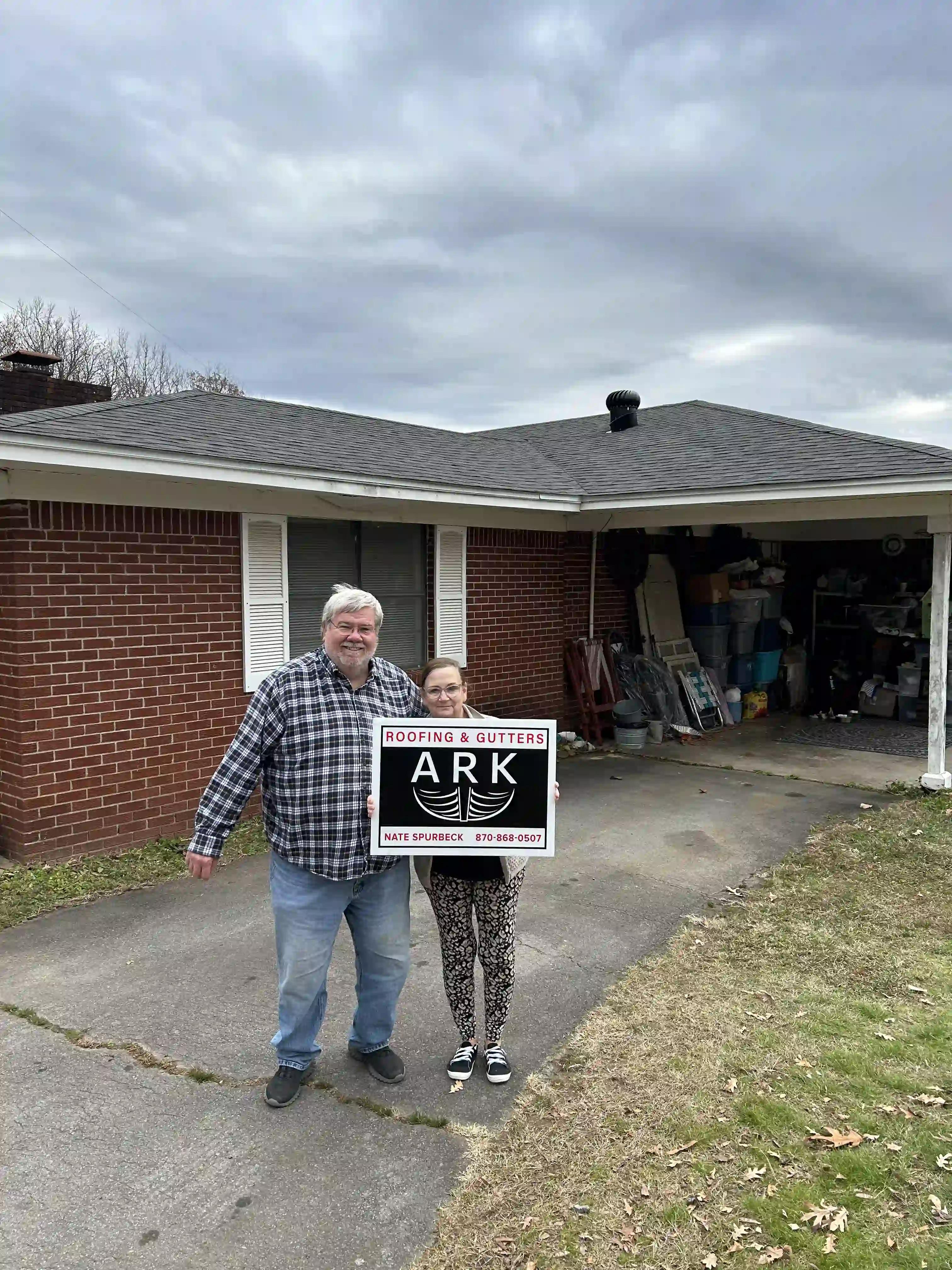 Arkadelphia homeowners standing in their driveway with an Ark Roofing and Gutters yard sign
